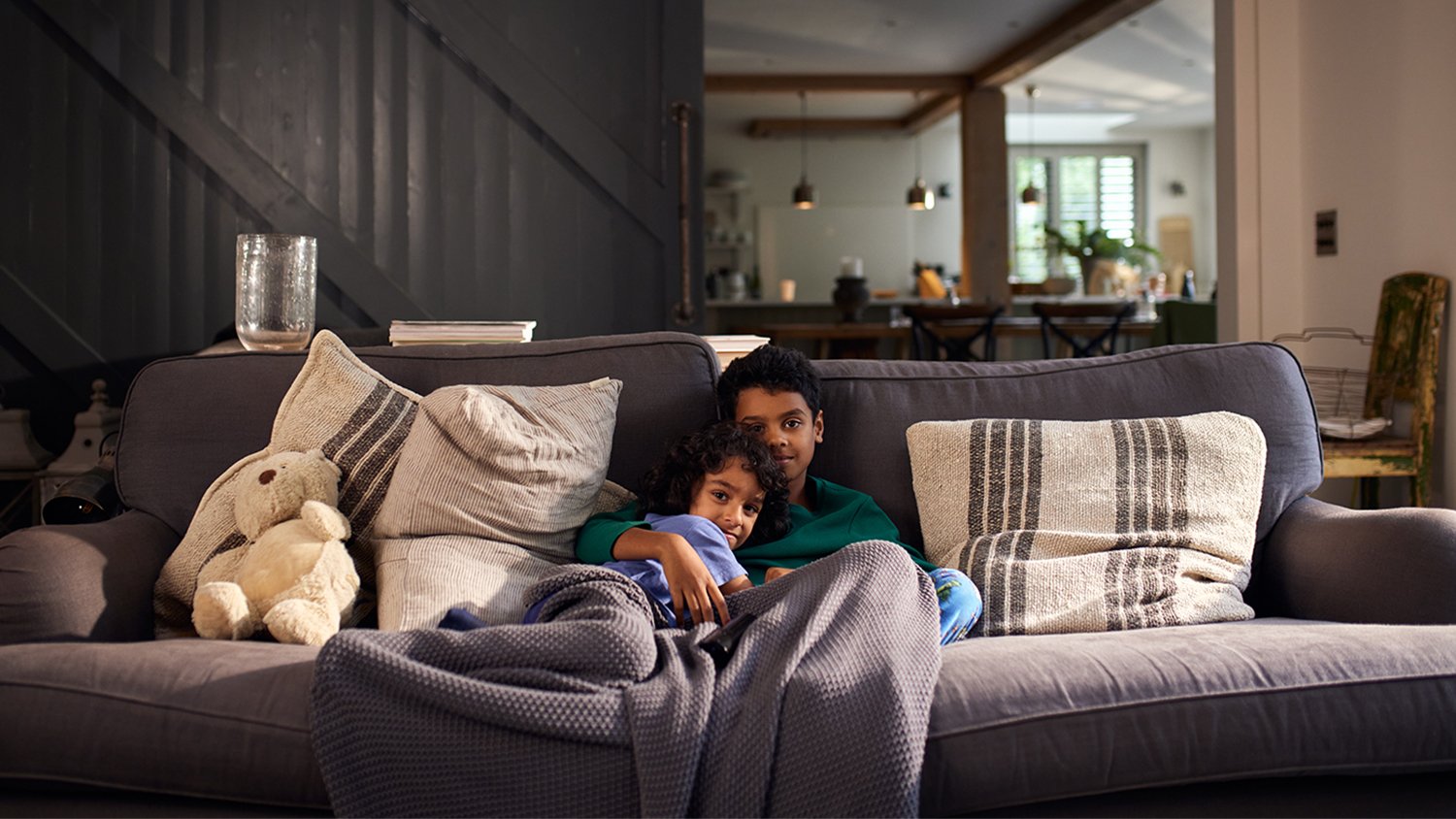 2 boys cozy together on couch with blanket